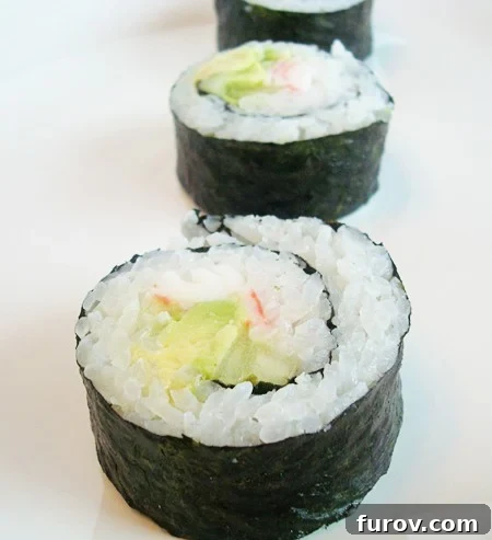 Three California sushi rolls neatly arranged in a row on a pristine white plate, showcasing the vibrant green avocado, white rice, and nori.