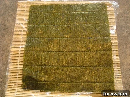 A sheet of dark green nori seaweed laid flat on the plastic-covered bamboo rolling mat.