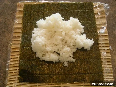 A mound of prepared white sushi rice placed in the center of a nori sheet, which rests on the bamboo mat.