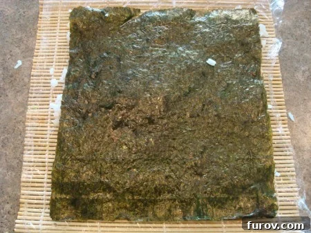 The nori sheet, now covered with rice on one side, has been flipped over on the bamboo mat, with the rice facing down.