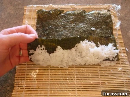 A slight lift of the nori sheet, revealing the white sushi rice layer underneath, confirming the roll is set up for an inside-out design.