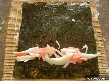 Thin strips of imitation crab meat arranged in a line on the nori sheet, positioned towards the bottom edge.