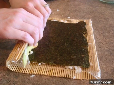 The initial stage of rolling a California sushi roll: the bamboo mat is lifted and folded over the ingredients, gently starting the roll.
