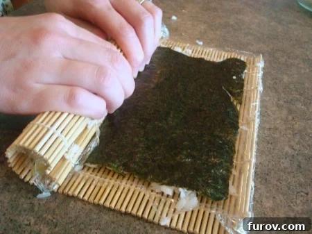 The California sushi roll being further tightened and rolled using the bamboo mat, creating a compact cylinder.