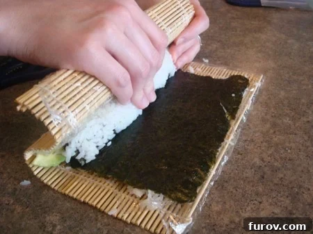 The bamboo mat pressing down on the sushi roll, with white rice visible on the outside, to compact and shape it further.