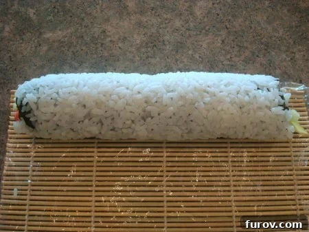 A fully formed California sushi roll, tightly wrapped within the bamboo mat, signifying the completion of the rolling process.