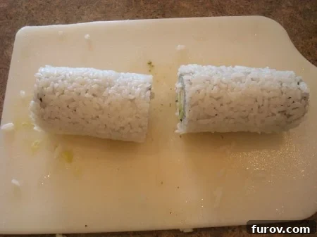 A long California sushi roll, with rice on the outside, carefully cut in half on a white cutting board.