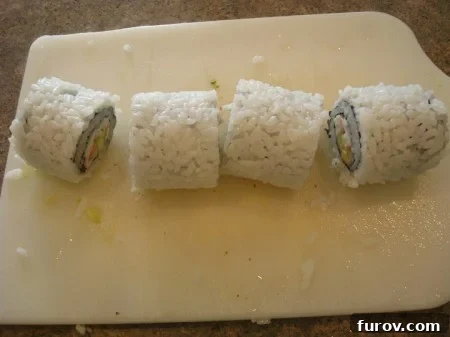 The two halves of the California sushi roll now cut into four distinct pieces on the white cutting board.
