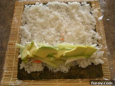 A nori sheet covered with white sushi rice, and then layered with avocado and crab meat directly on top, for a nori-outside roll.