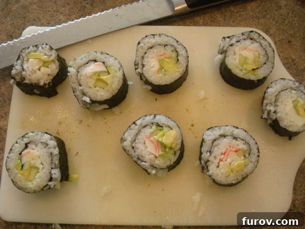 A white cutting board displaying neatly sliced pieces of California sushi roll with the dark nori seaweed visible on the outside.