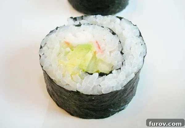 A close-up, top-down view of a freshly prepared California sushi roll resting on a simple white plate, ready to be sliced and served.