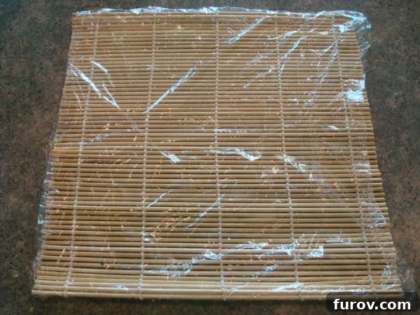 A bamboo mat laid flat, covered neatly with a layer of plastic wrap, extending slightly beyond the edges.