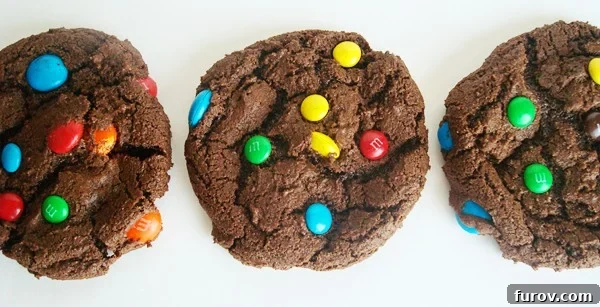 Three chocolate M&M cookies lined up in a row, showcasing their rich, dark color and colorful candy pieces.