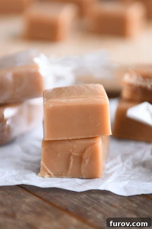 Soft and chewy homemade caramels stacked on one another on parchment paper, glistening with rich flavor.