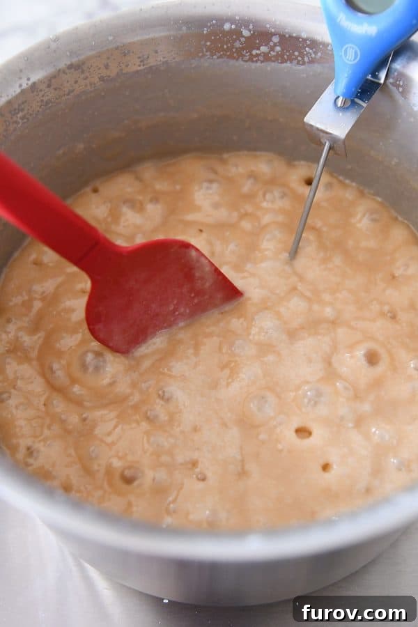 Bubbling caramel being actively cooked and stirred with a red spatula, a crucial step for achieving perfect consistency.