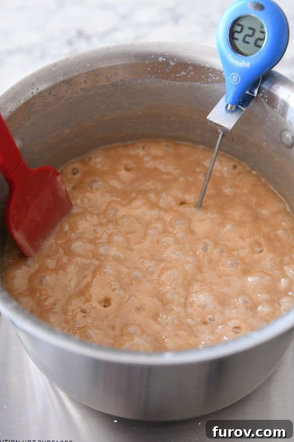 Caramels cooking to 245 degrees in a metal pot, continuously stirred with a red spatula to prevent burning.
