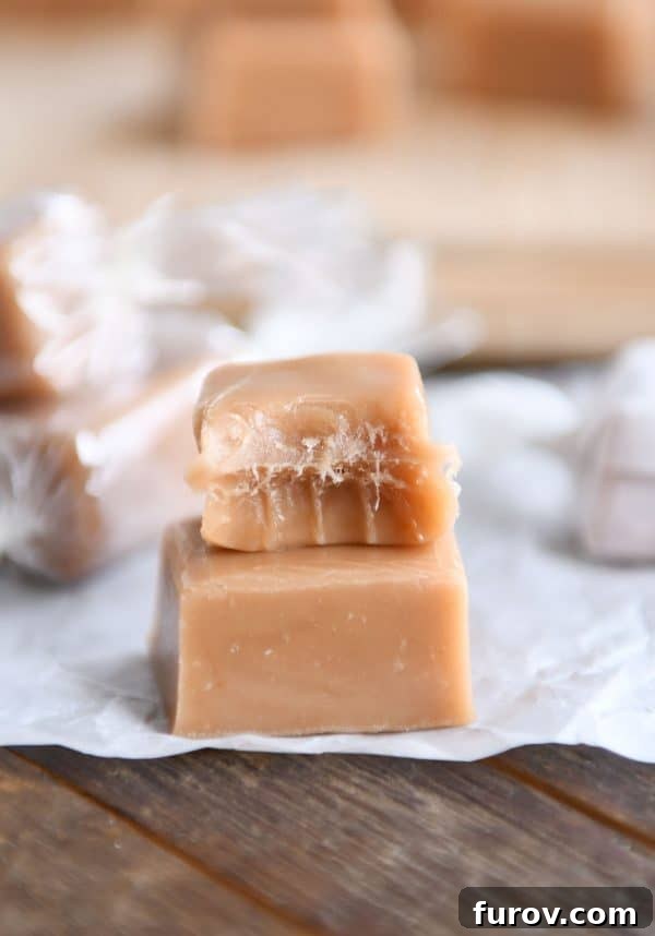Two soft and chewy homemade caramels stacked on parchment paper, with one having a delicious bite taken out.
