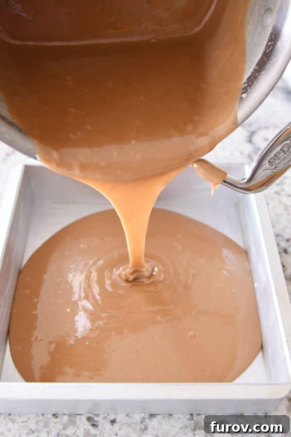 Hot caramel being carefully poured into a metal pan, a critical step before cooling and cutting.