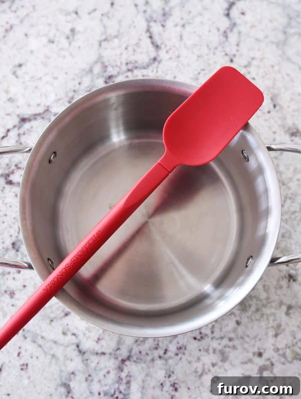 A heavy-bottomed pot and a red flat-edge spatula, essential tools for making delicious homemade caramels.