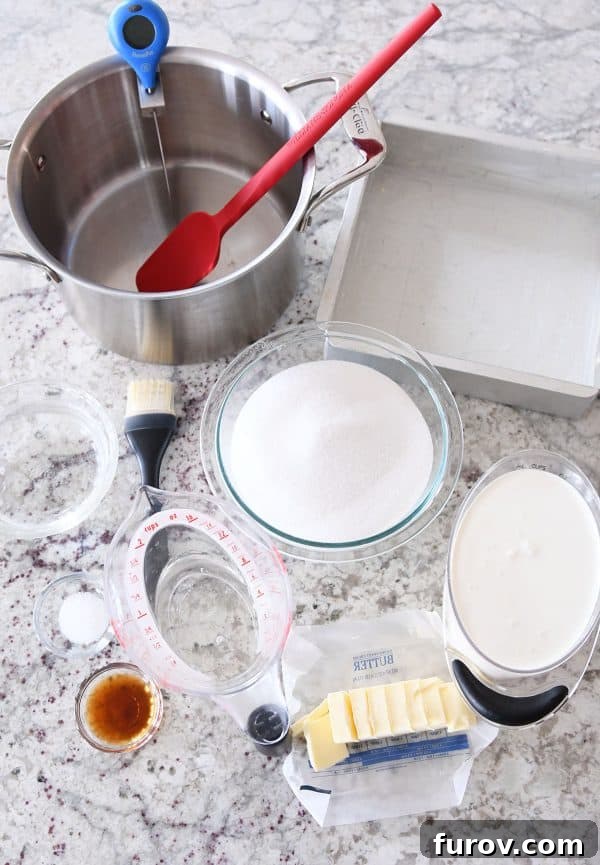 All caramel making supplies laid out: pot, spatula, sugar, cream, butter, vanilla, and thermometer, ready for use.