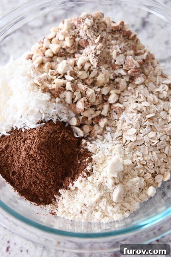Dry ingredients for dark chocolate brownie granola bars, including oats, cocoa, almonds, and flour, in a clear glass bowl.