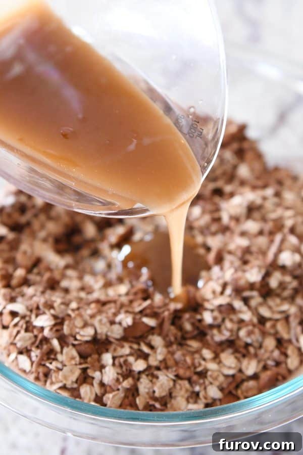 Thick, golden syrup being poured over the dry ingredients for dark chocolate brownie granola bars in a mixing bowl.
