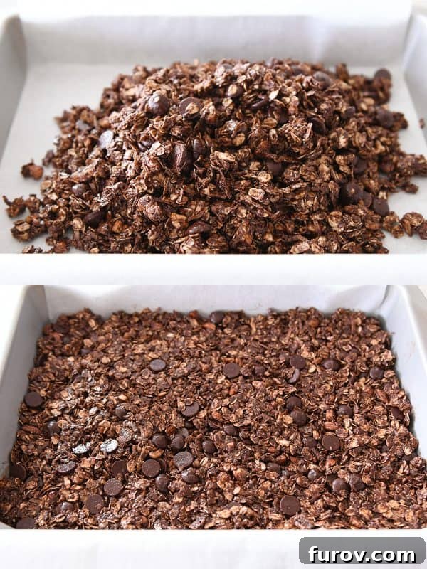 A hand gently pressing the dark chocolate brownie granola bar mixture into a parchment-lined 9x13-inch pan.