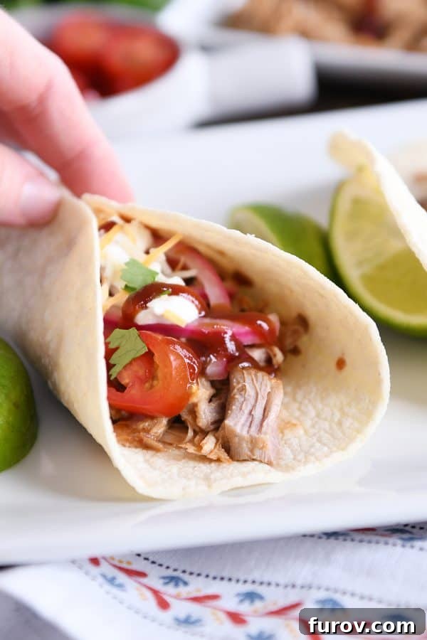 Ultimate Instant Pot BBQ Pork Tacos 9 A hand gently holding a vibrant Instant Pot BBQ pork taco, adorned with crisp pickled onions and a glossy BBQ sauce drizzle, against a blurred background.