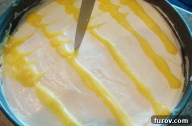 Close-up of a paring knife gently dragging through lines of lemon curd on top of a cheesecake, creating a decorative swirled pattern.