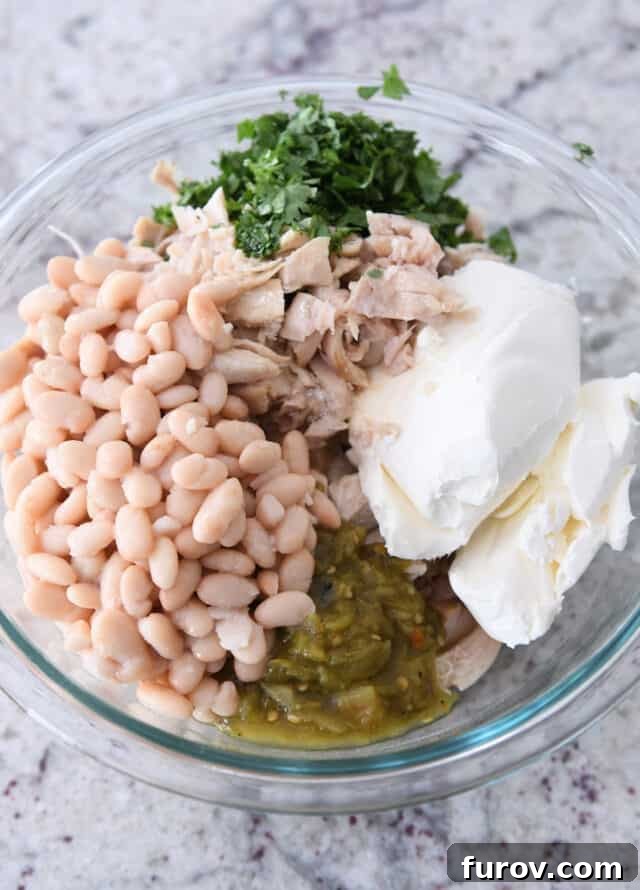 Glass bowl with white beans, green chiles, cream cheese, chicken, cilantro.