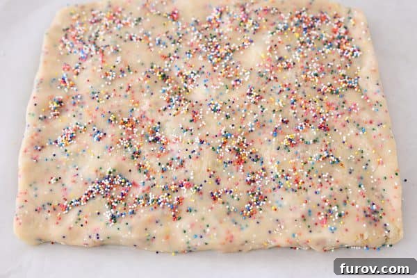 The flattened shortbread dough rectangle, evenly topped with an extra layer of colorful sprinkles, awaiting refrigeration.