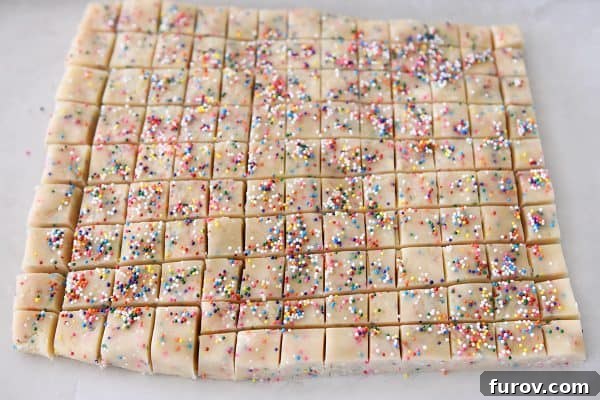A sharp knife cutting the chilled funfetti shortbread dough into small, evenly sized squares on a baking sheet.