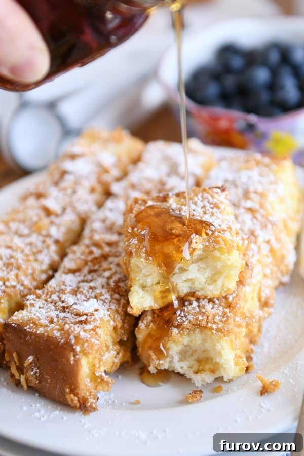 Crunchy baked french toast sticks with syrup getting poured on top.