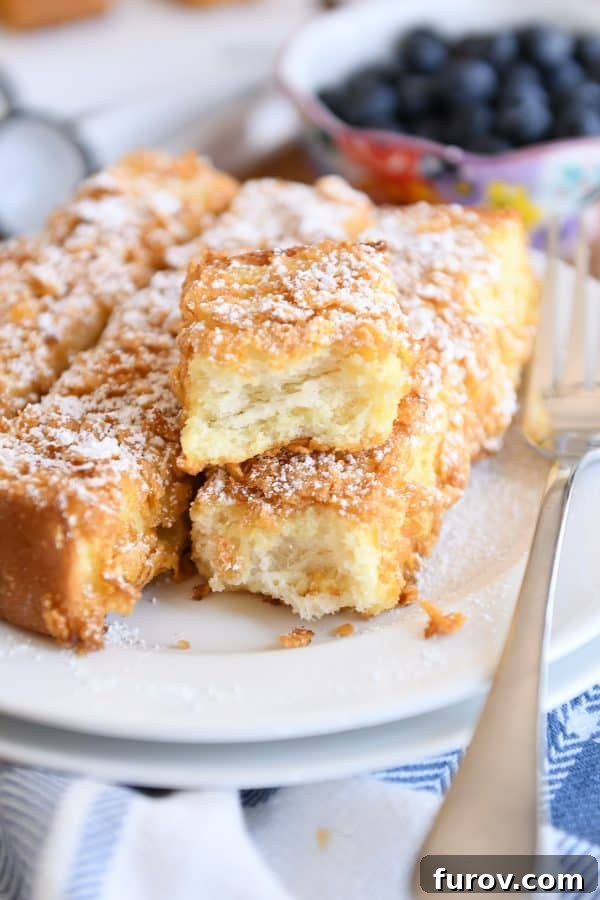 Crunchy baked french toast sticks with powdered sugar on white plate.