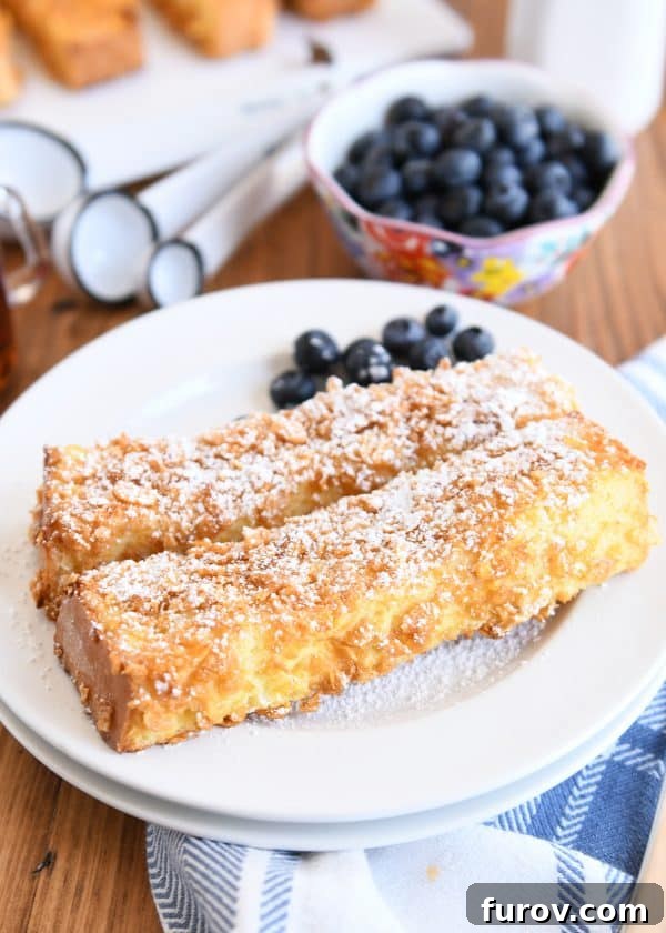 Two crunchy baked french toast sticks on white plate with powdered sugar and blueberries.