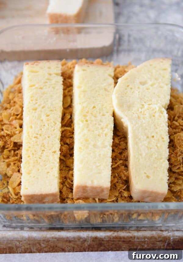 Pressing buttery corn flakes on dipped french toast sticks.