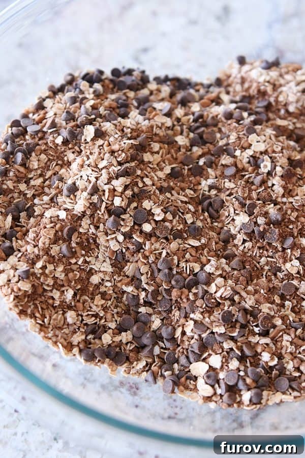 Mini chocolate chips are perfectly mixed into the dry granola ingredients, ready for the next step in making chocolate peanut butter brownie granola bites.