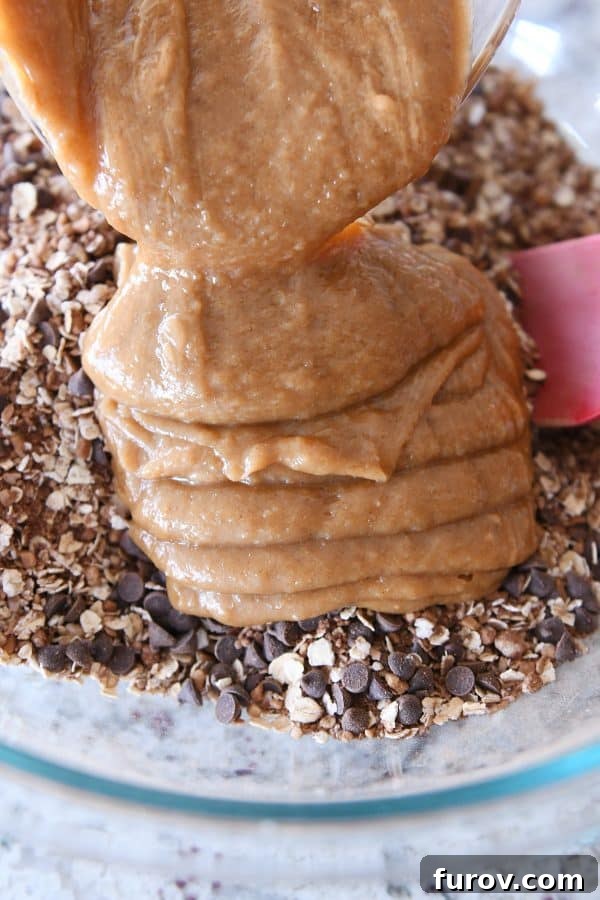 Pouring the rich, creamy peanut butter syrup into the bowl of dry granola mixture, ready to be combined.
