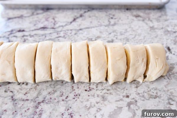Perfected Homemade Orange Sweet Rolls 8 A log of orange sweet roll dough, expertly sliced into uniform circles, ready for shaping.
