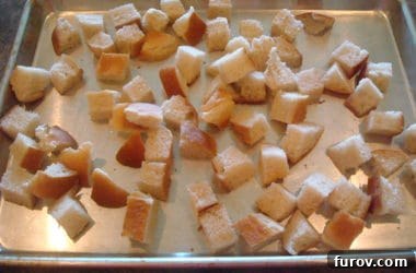 Unbaked bread cubes meticulously spread in a single layer on a metal cookie sheet, ready to be seasoned and placed into the oven for toasting.