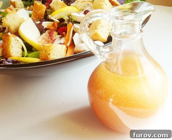 Small glass pitcher of homemade red wine vinaigrette next to a large bowl of gourmet green salad.