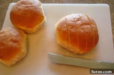Slicing fresh bread rolls into uniform ½-inch strips on a white cutting board, preparing them for the next step in making homemade croutons.