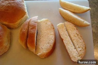 A roll that has been cut into ½-inch strips, now being sliced in half lengthwise on a white cutting board to create thinner pieces suitable for croutons.