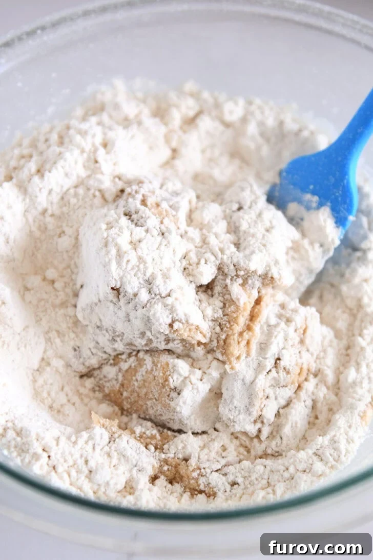 A glass bowl with flour being gently mixed into cookie dough.