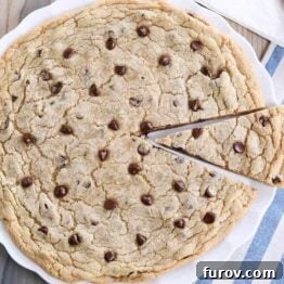 Giant chocolate chip cookie on white platter with slice cut.