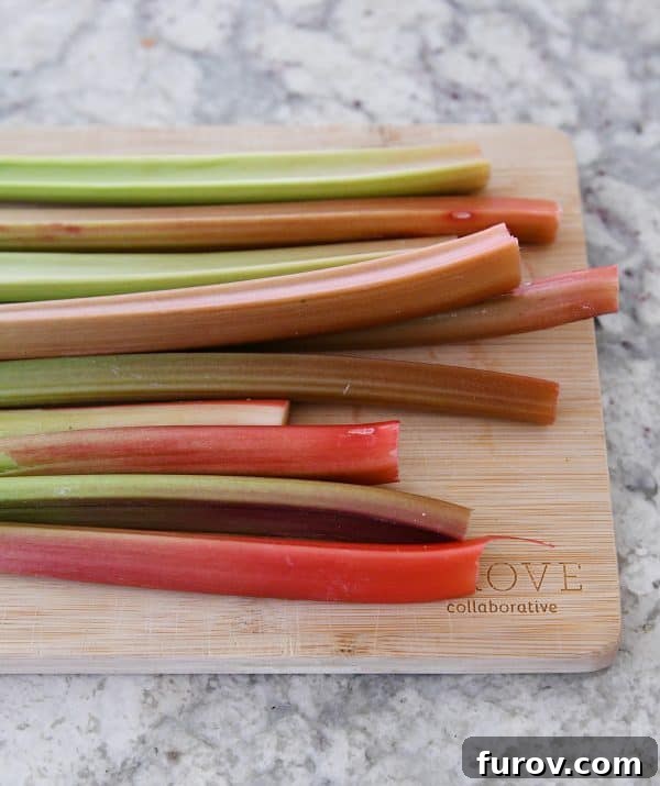 Tangy Rhubarb Custard Delight 7 Several stalks of fresh rhubarb, varying in color from green to reddish-pink, are laid out on a rustic wooden cutting board, ready for trimming and slicing.