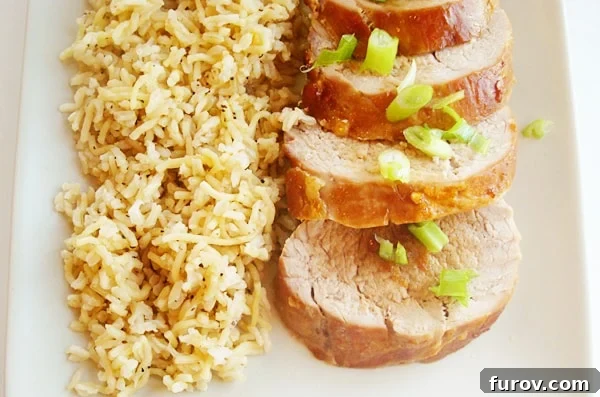 Thinly sliced Asian glazed pork tenderloin artfully arranged next to a mound of fluffy brown rice on a white platter, garnished with green onions.
