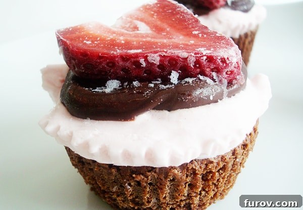 A beautifully presented chocolate cupcake topped with a swirl of whipped cream, drizzled with chocolate sauce, and garnished with a fresh sliced strawberry, ready to be enjoyed.
