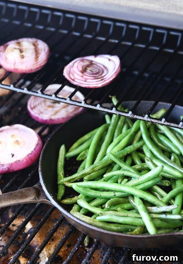 Fresh green beans sizzling in a cast iron skillet placed on a hot grill, showing a slight char.