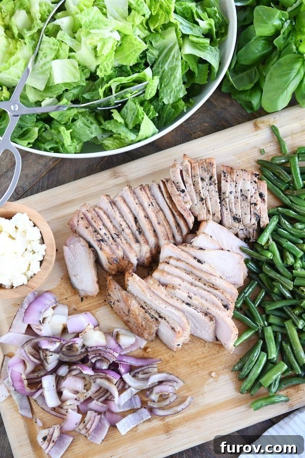An overhead view of a deconstructed grilled pork salad, featuring perfectly grilled pork, onions, green beans, and crumbled feta cheese.
